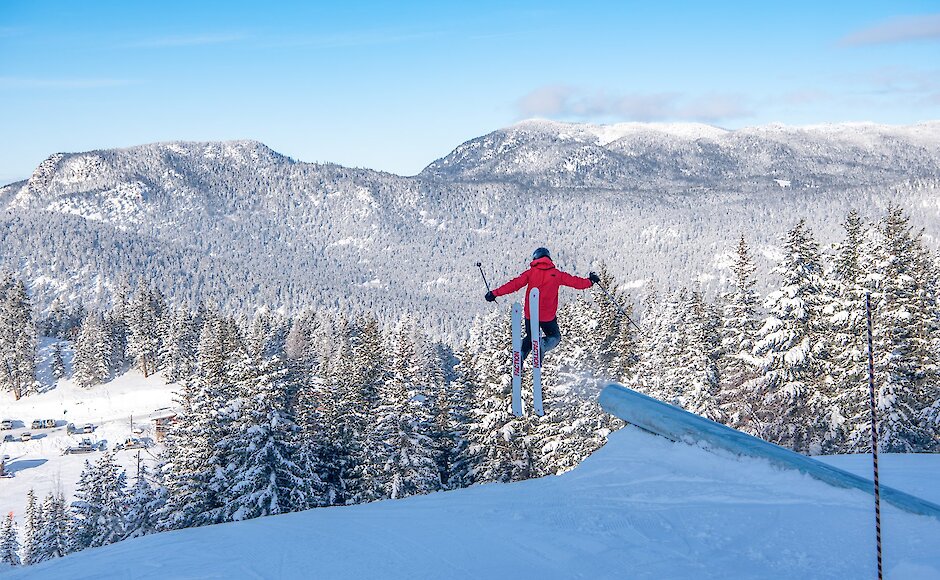 A skier going off a pipe jump with the snowy BC mountains in the background at Harper Mountain, near Kamloops, BC.