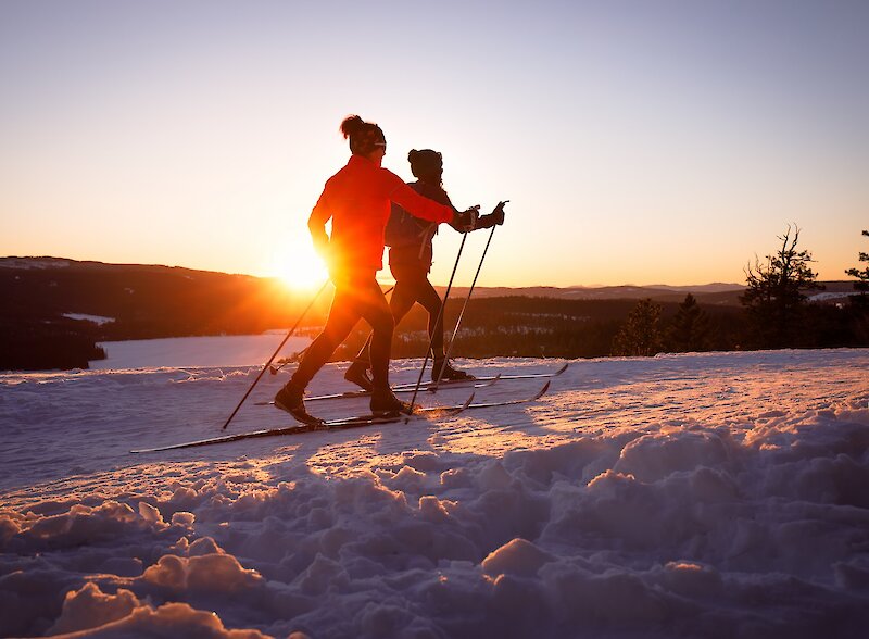 Two cross country skiers gliding on the trails at Stake Lake with the sunset in the background located near Kamloops, BC.