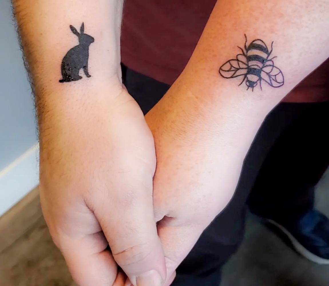 Oliver and Beth holding hands at Big Foot Tattoo. Oliver has a black bunny while Beth has a bumble bee