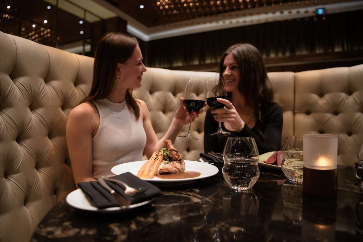 Two women drinking wine with their meal at Atlas Steak + Fish Restaurant in Kamloops, BC.