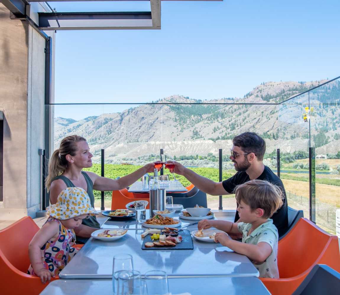 A family with the parents enjoying a glass of wine and lunch on the scenic Monte Creek Winery Patio located in Kamloops, British Columbia.