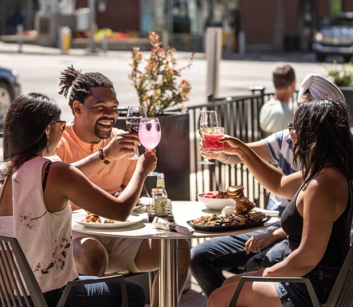 Group of people cheers-ing their drinks on the sunny Cordo Resto + Bar patio located in downtown Kamloops, British Columbia.