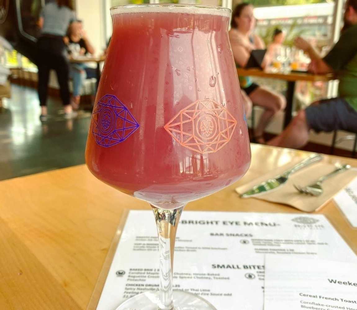 a glass of blueberry julius beer from bright eye brewing on a table with menu