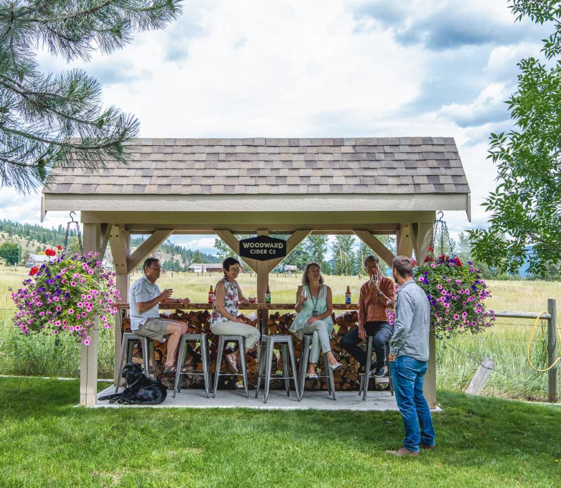 A group of people enjoying ciders at an outdoor bar table at Woodward Cider Co. in Kamloops, BC.