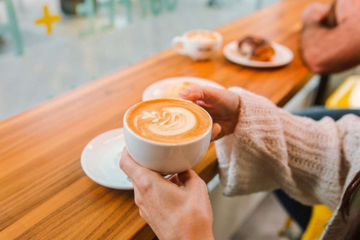 two hands picking up a coffee cup at Amplified Cafe in downtown Kamloops