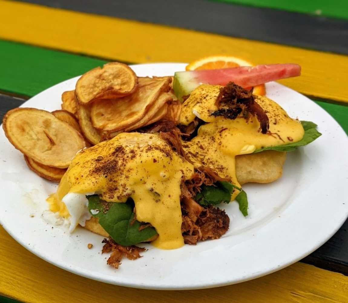 eggs benedict with jerk chicken and hollandaise on a plate set on a striped table