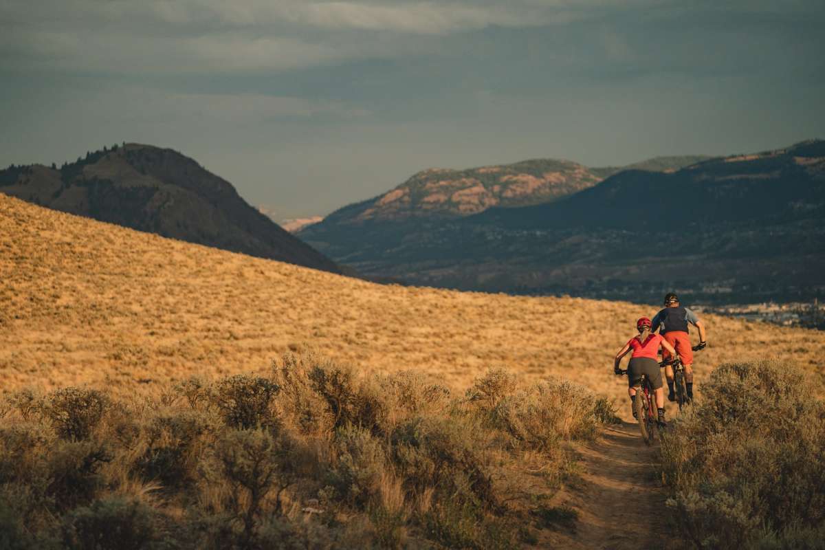 A couple mountain biking through the Lac du Bois Grasslands with scenic mountains in the background in Kamloops, British Columbia.