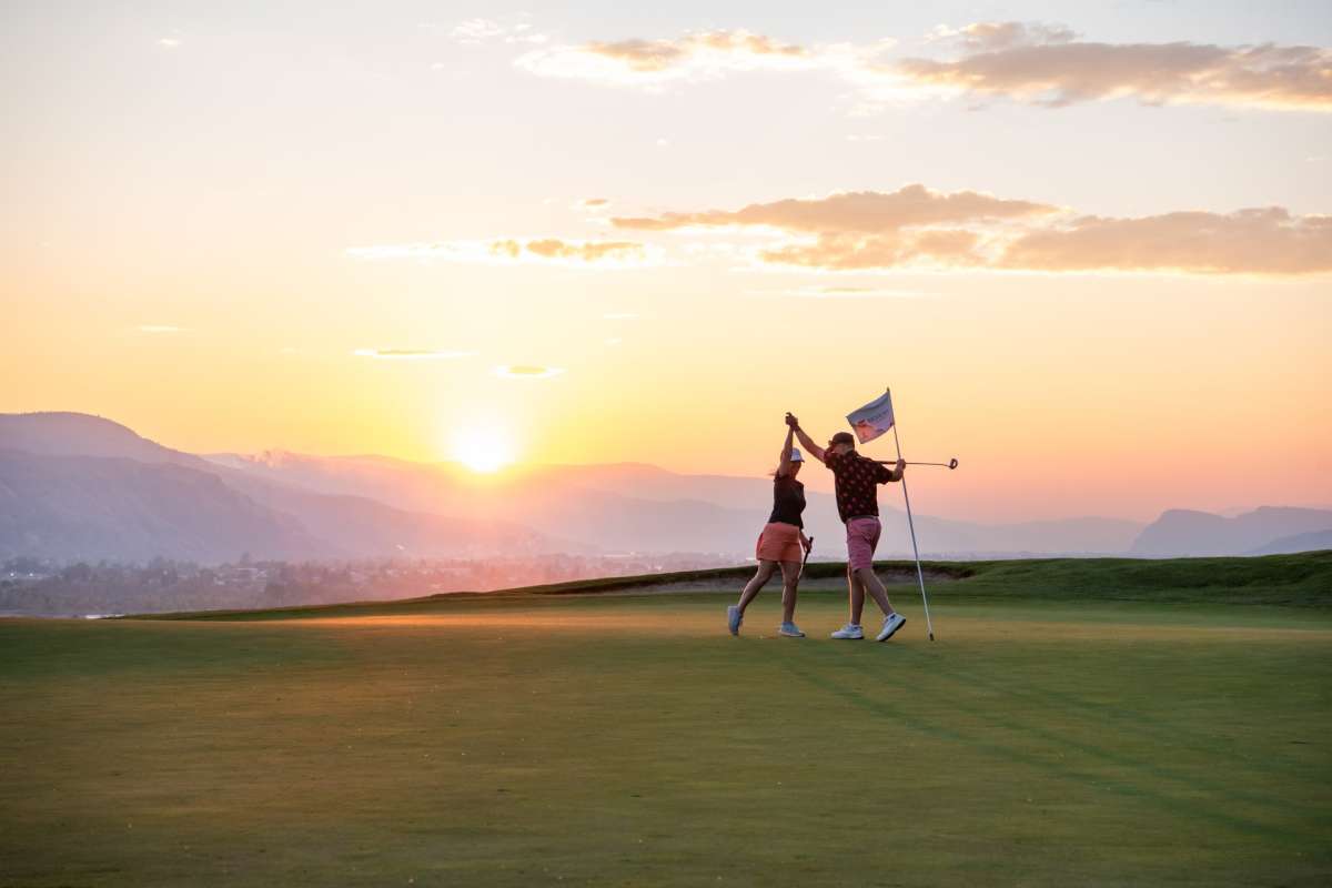 Two golfers high-fiving on the golf green with the sunset in the background at the Bighorn Golf & Country Club in Kamloops BC.