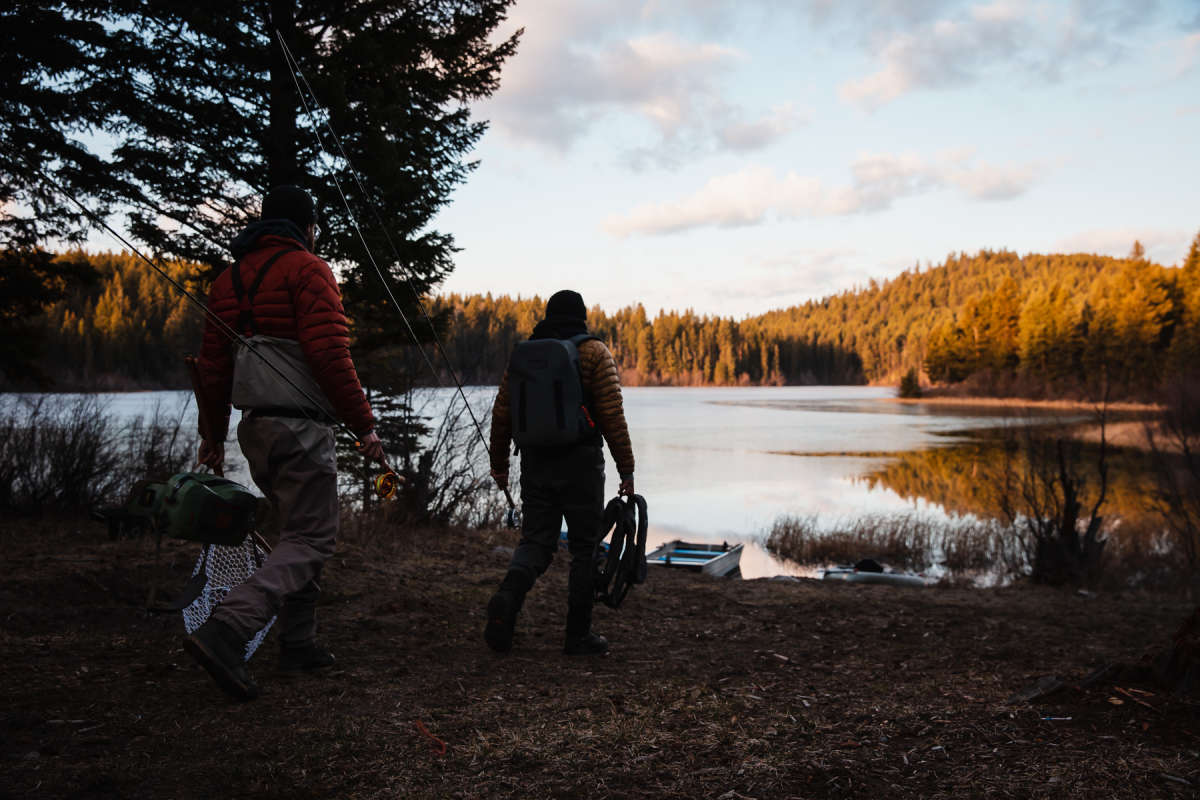 Two men carrying fishing tackle walking towards a partly frozen lake for ice off fishing in Kamloops, BC.