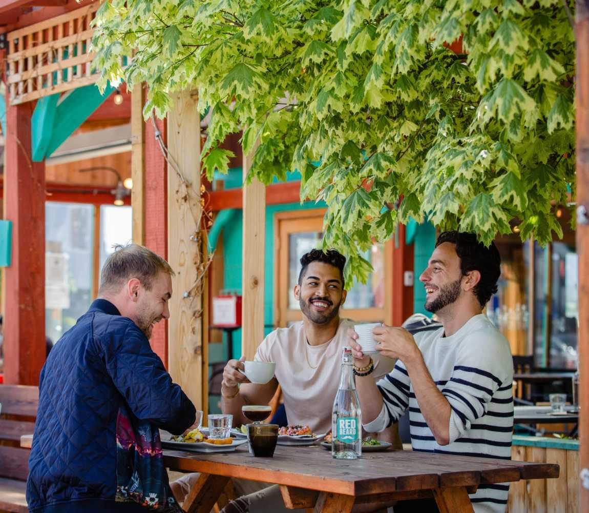 Three men dining and drinking coffee on the Red Beard Cafe Patio located on Kamloops North Shore, British Columbia.