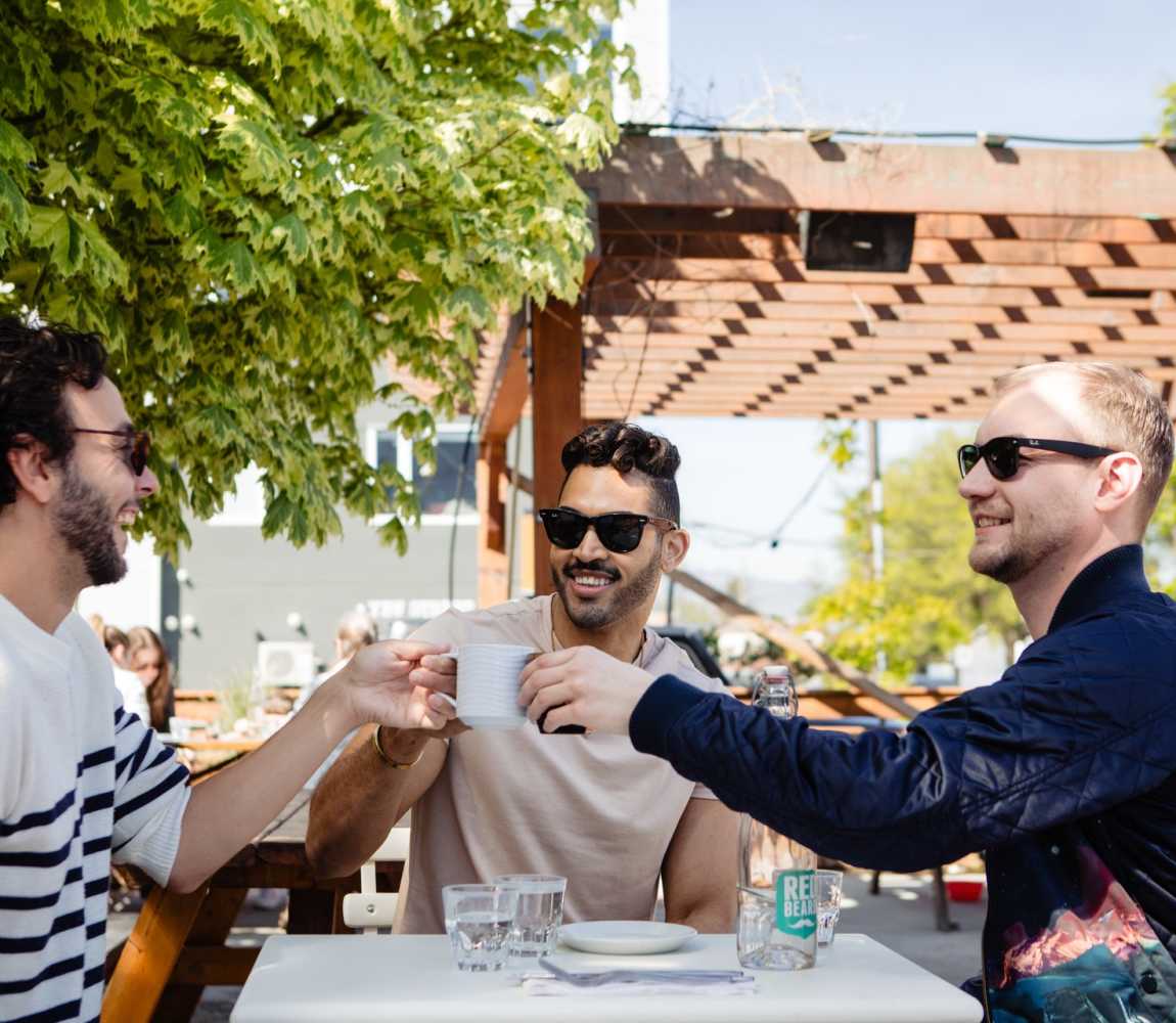 Three men cheers-ing their coffee on the patio at Red Beard Cafe in Kamloops, British Columbia.