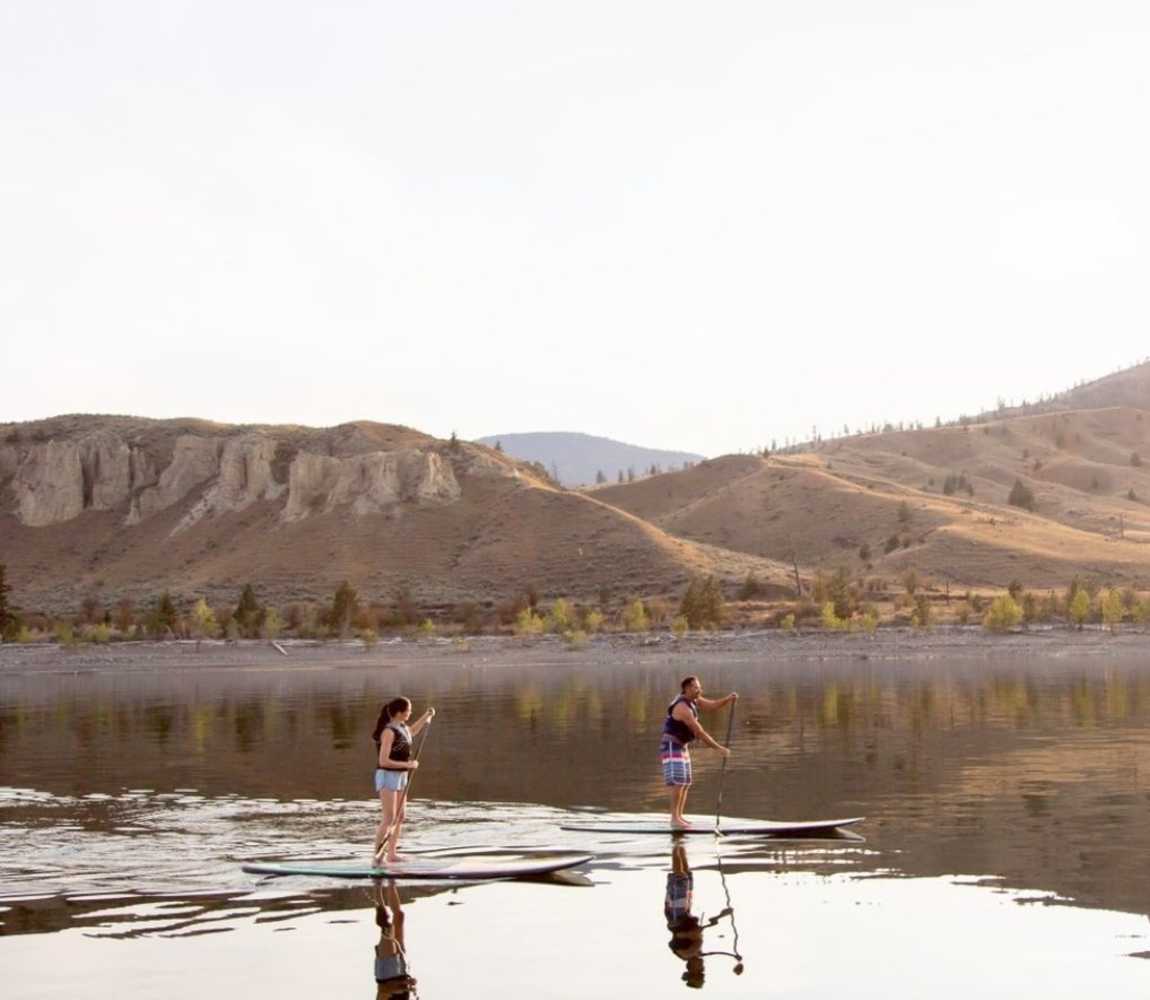 Two paddleboarders on Kamloops Lake surrounded by the natural beauty of the BC mountains in the background.