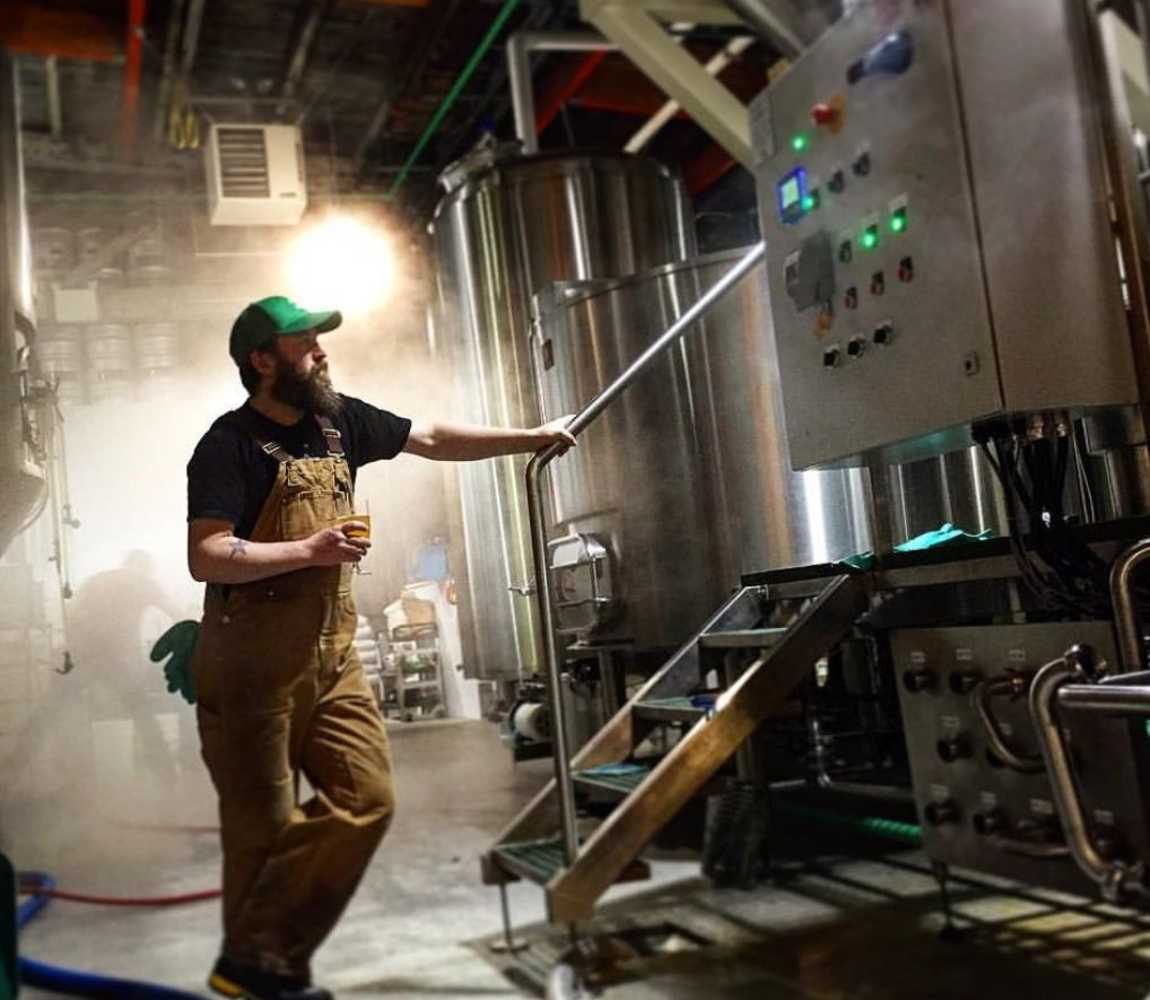 Iron Road Brewing brewer, Aaron MacInnis, holding a glass of beer looking at the brewer tank