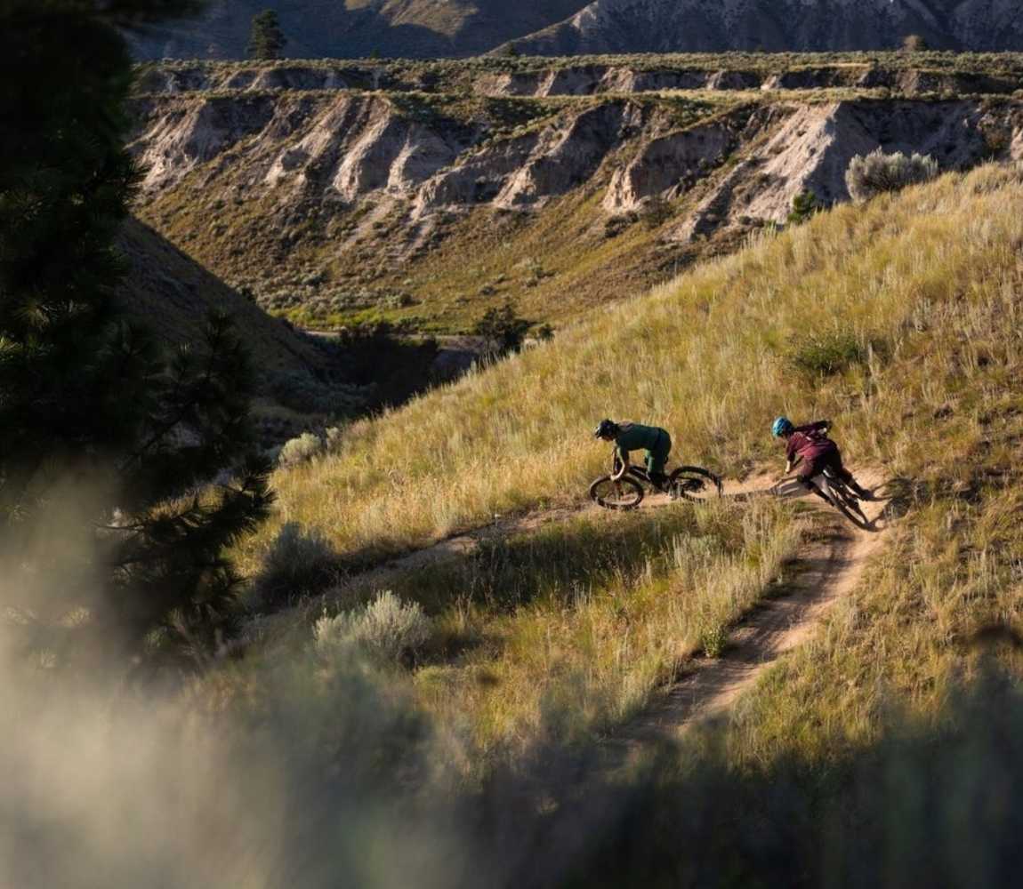 Two mountain bikers riding down a single track bike trail with picturesque canyons in the background at the Kamloops Bike Ranch.