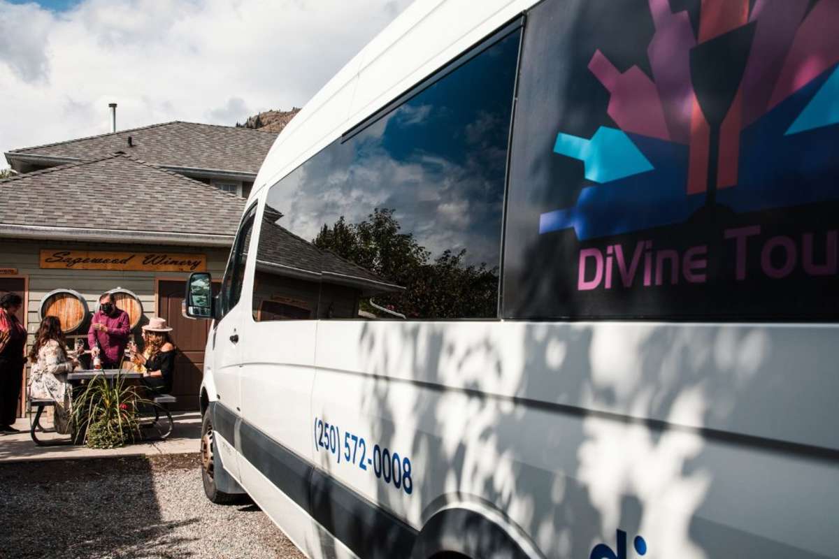 divine tours van outside a winery with four people on a patio in kamloops