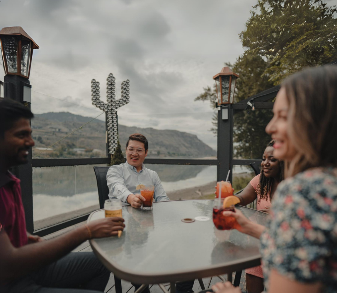 Group of people enjoying their cocktails on a riverside patio at the Sandbar and Grill in Kamloops, BC.