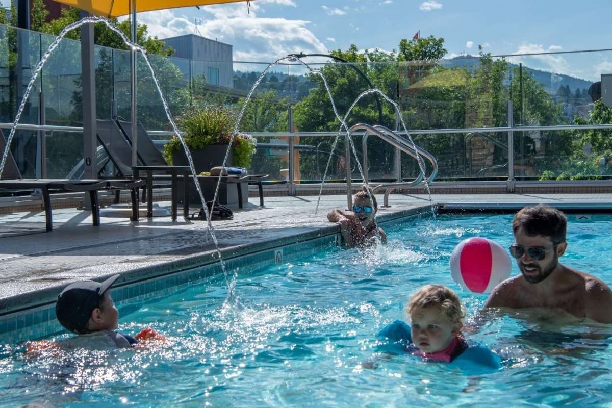 two kids and two adults swimming in outdoor rooftop pool with a yellow umbrella