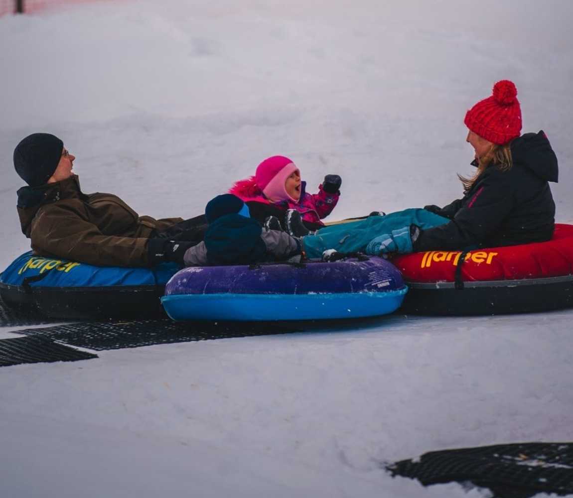 3 individuals tubing down a snowy hillside