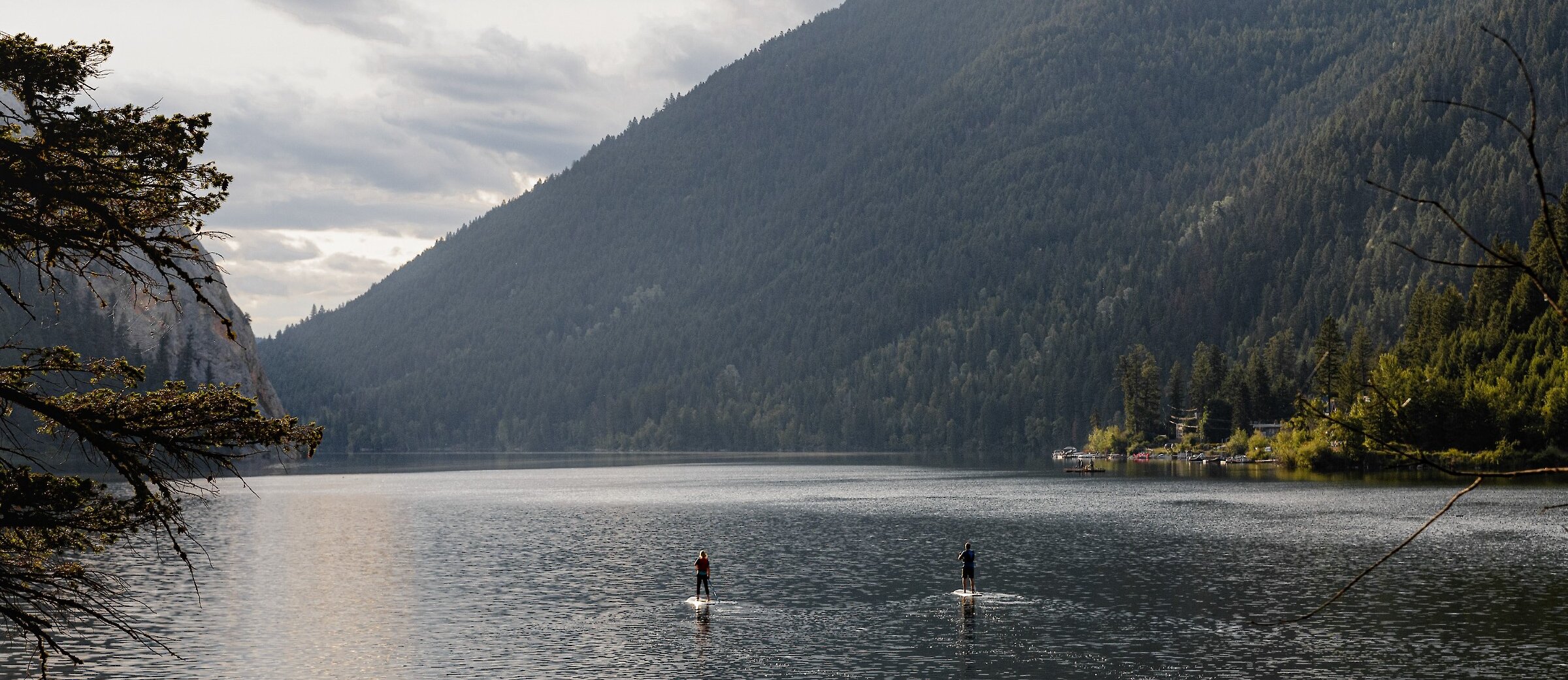 A couple paddleboarding on Paul Lake surrounded by lush greenery located near Kamloops British Columbia.