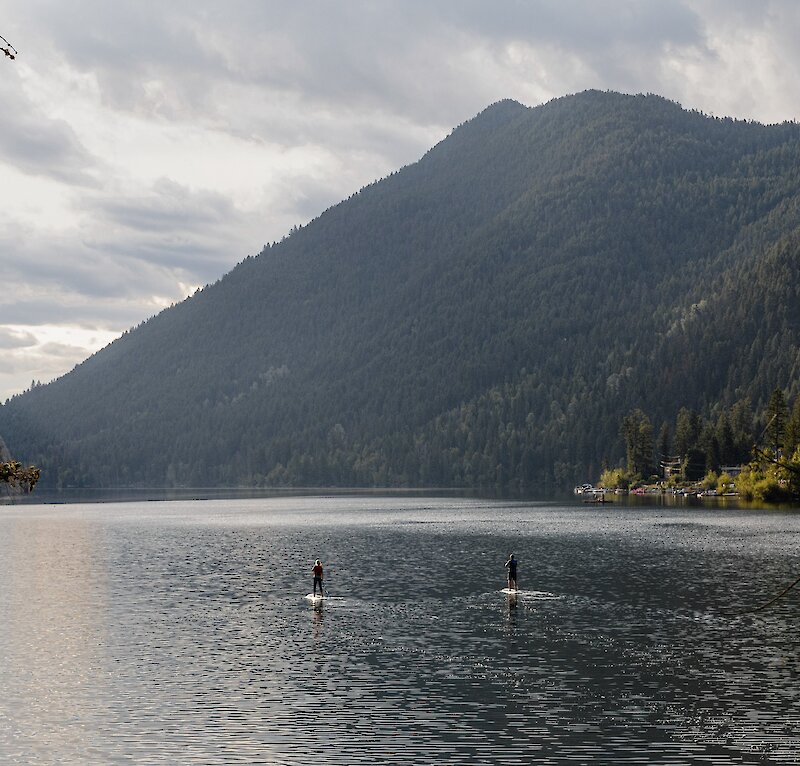 A couple paddleboarding on Paul Lake surrounded by lush greenery located near Kamloops British Columbia.