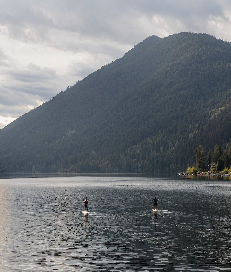 A couple paddleboarding on Paul Lake surrounded by lush greenery located near Kamloops British Columbia.