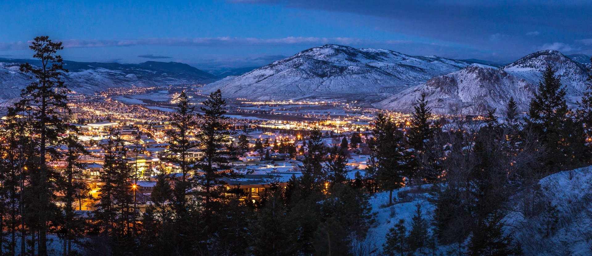 The city of Kamloops seen at night, nestled among snowy hills.