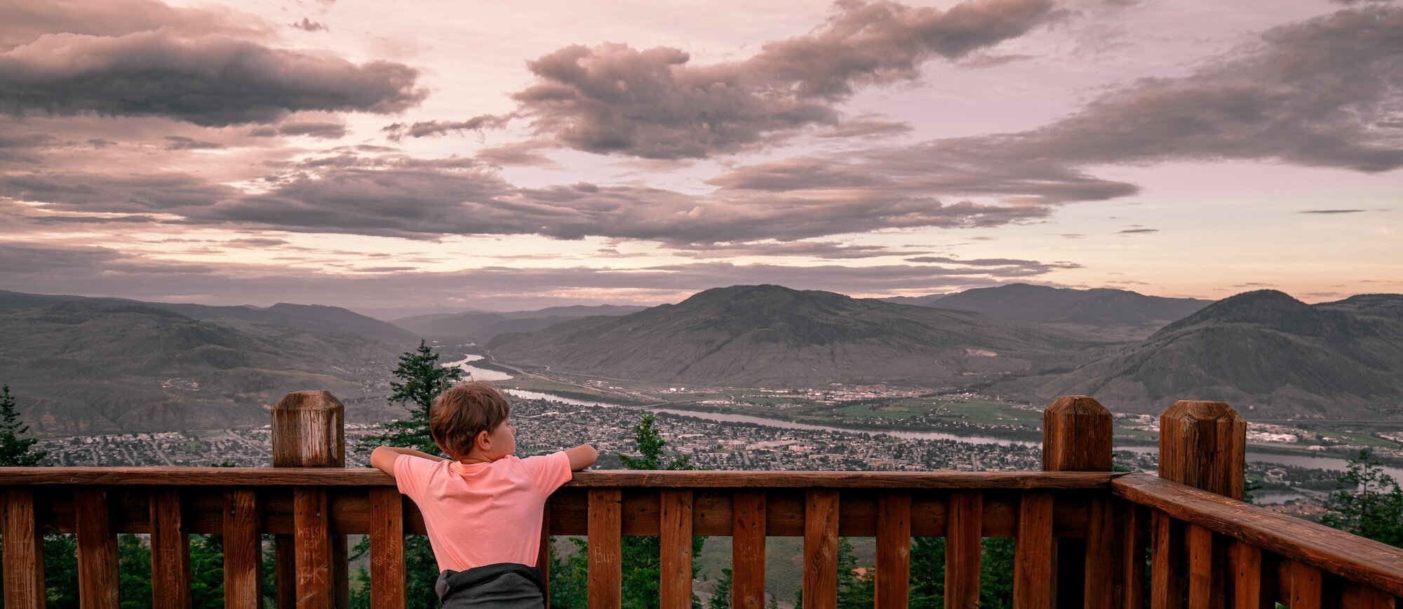 Boy admiring the view of city from Tower Trail lookout at Kenna Cartwright Park in Kamloops, BC.