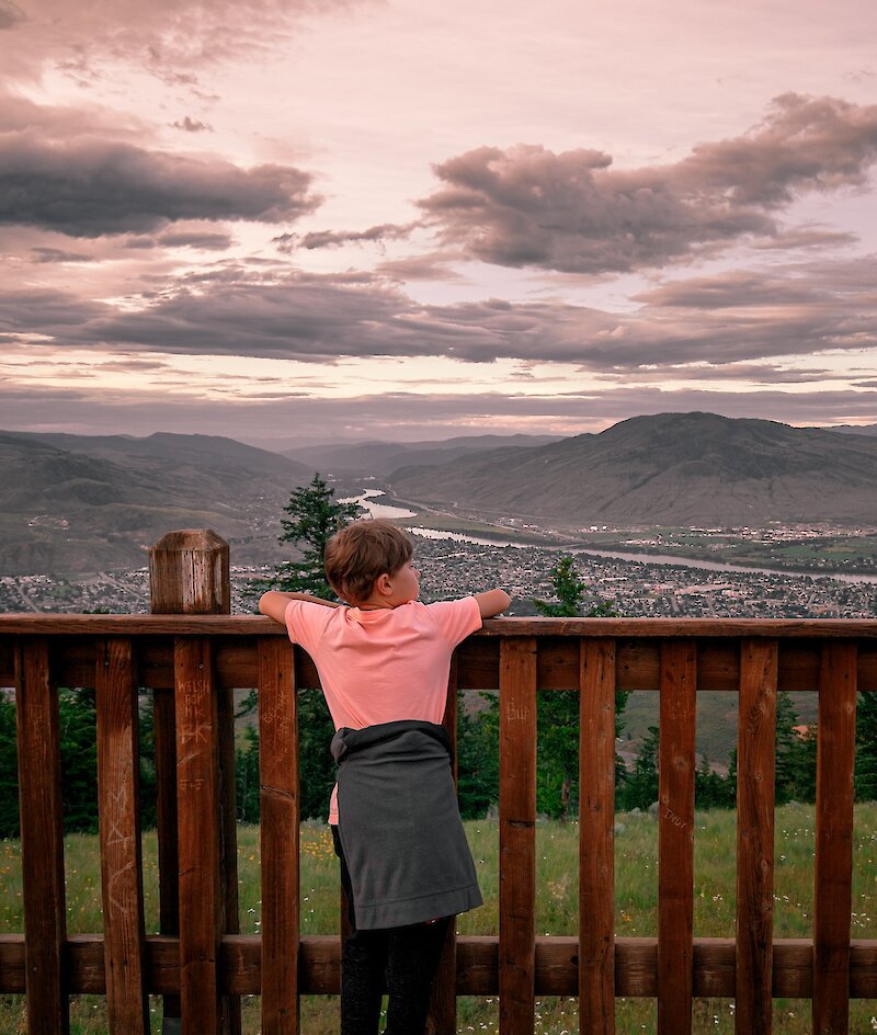 Boy admiring the view of city from Tower Trail lookout at Kenna Cartwright Park in Kamloops, BC.