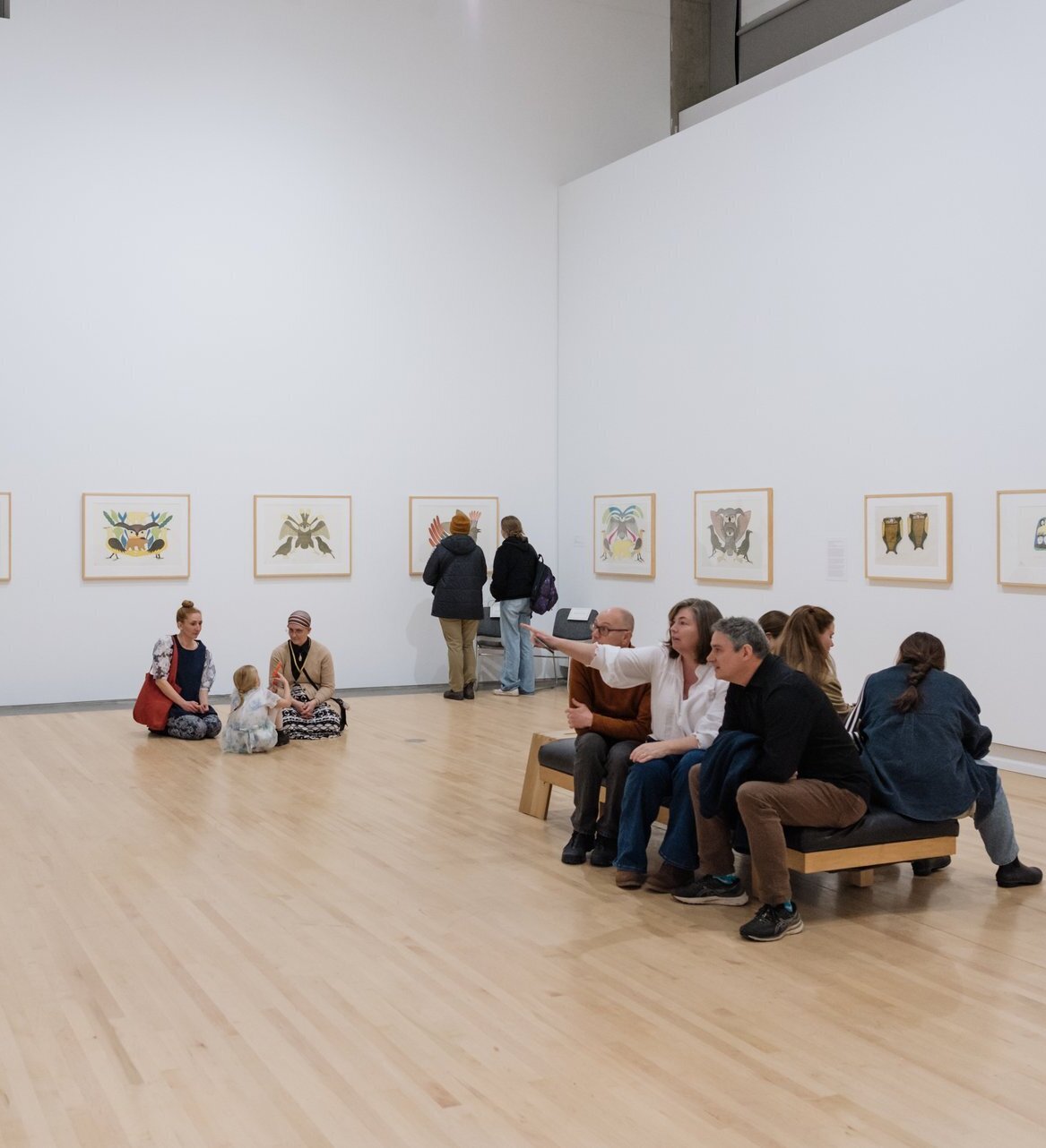 A group of people sit inside an art gallery, considering a range of indigenous art prints.