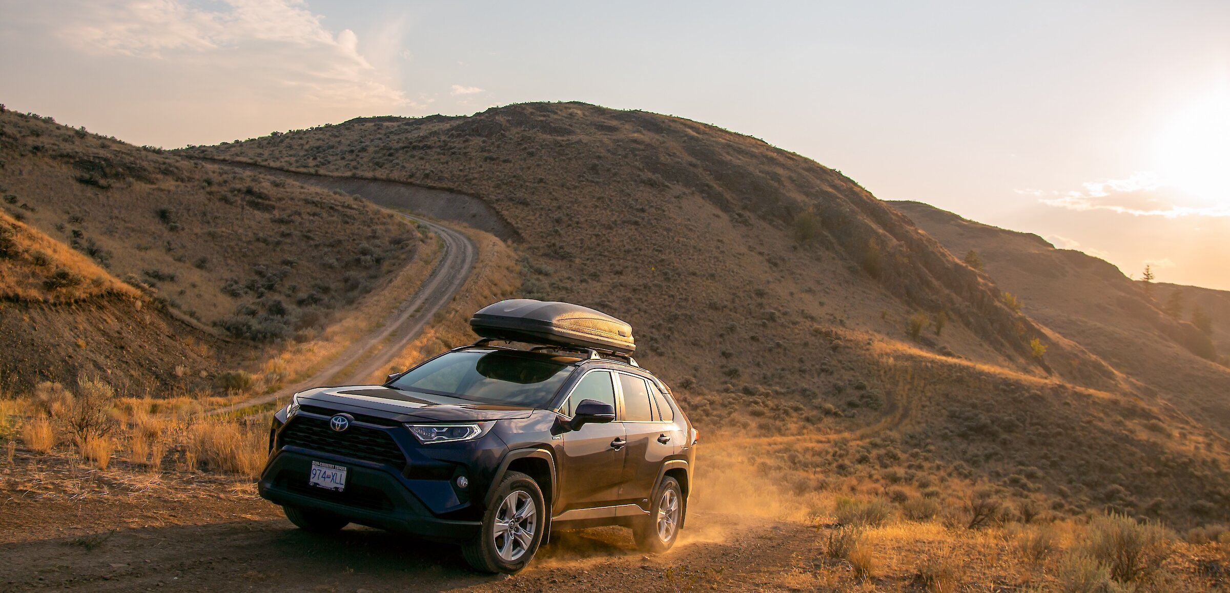 A Rav4 driving up a dirt road surrounded by golden grasslands in Kamloops, BC.