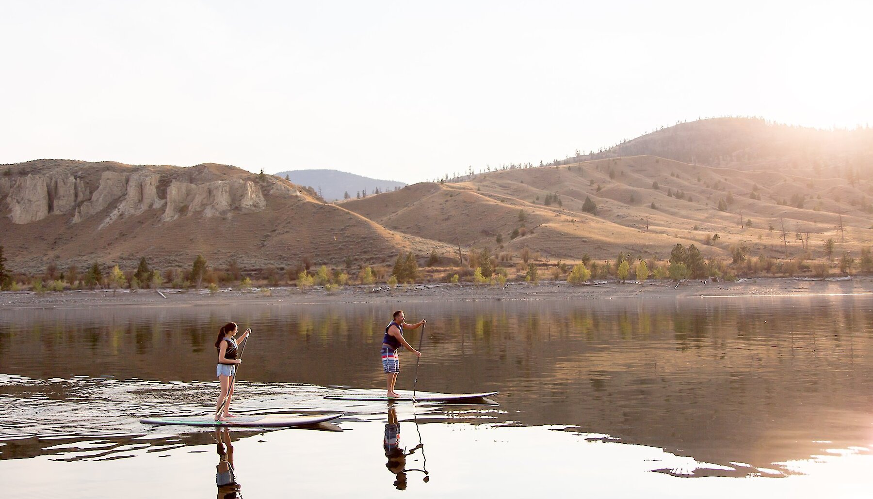 Two paddleboarders on Kamloops Lake surrounded by the natural beauty of the BC mountains in the background.