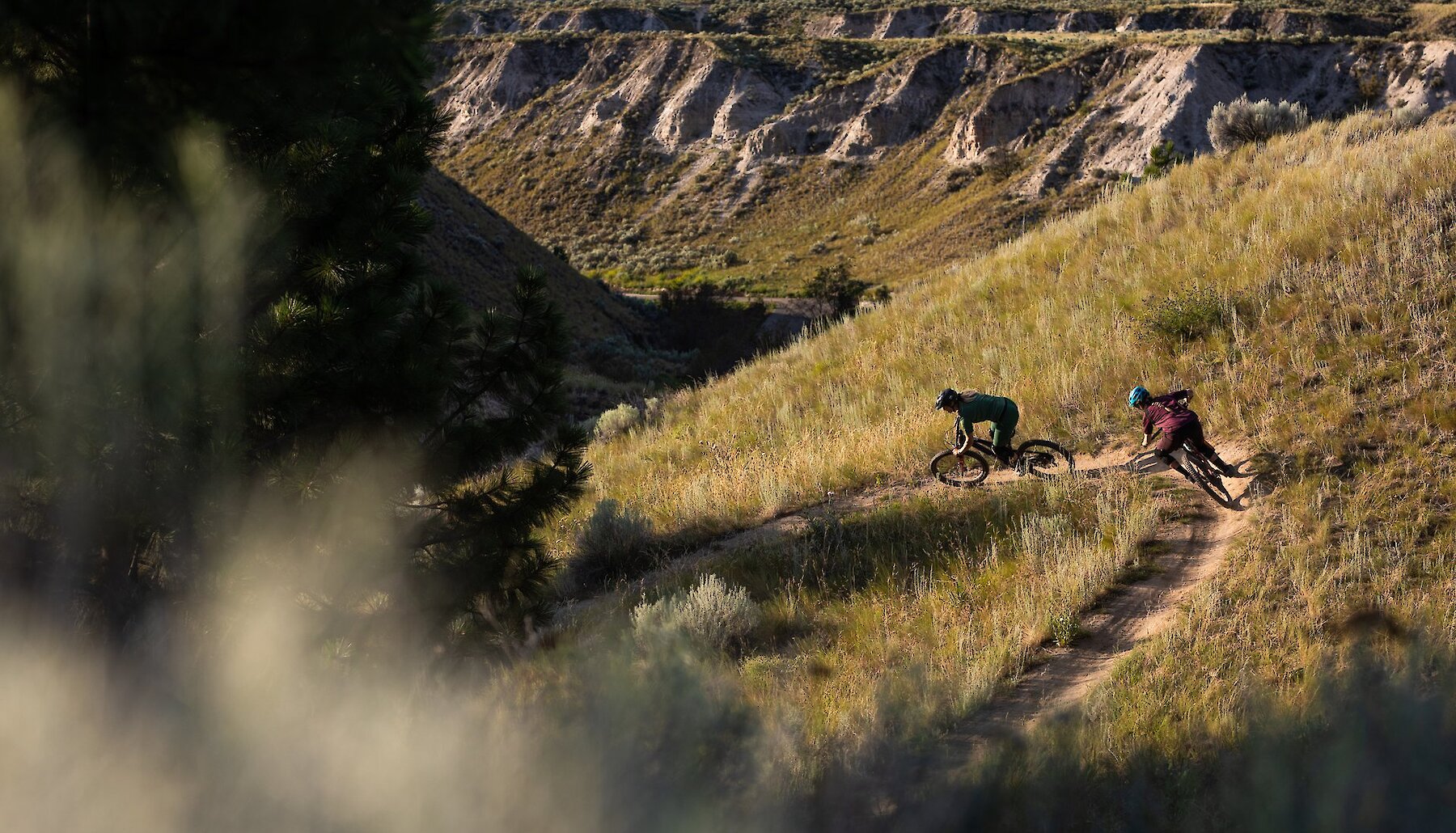 Two mountain bikers riding down a single track bike trail with picturesque canyons in the background at the Kamloops Bike Ranch.