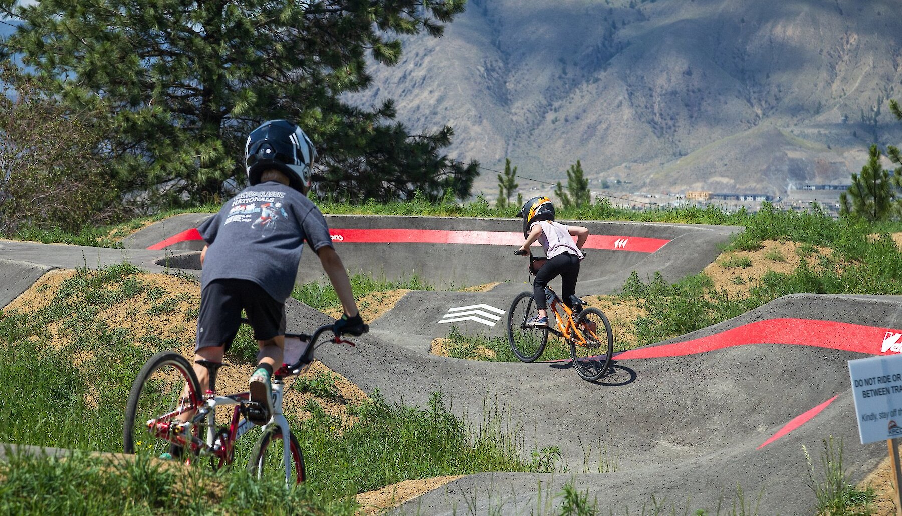 Two young bikers riding the accessible all wheels pump track at the Kamloops Bike Ranch.