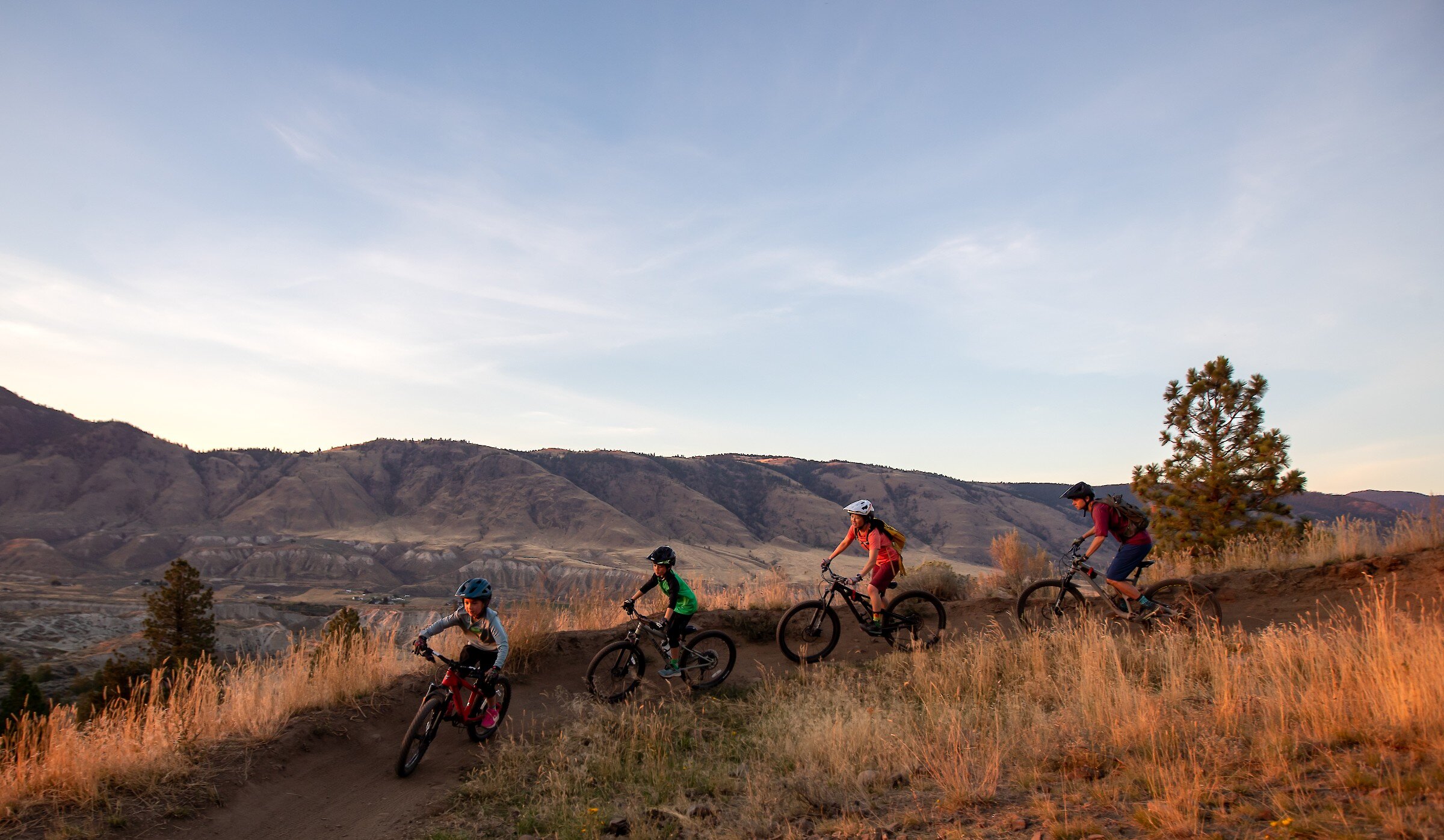 Family mountain biking along a bike trail at the Kamloops Bike Ranch with a view of the mountains in the background in Kamloops, British Columbia.