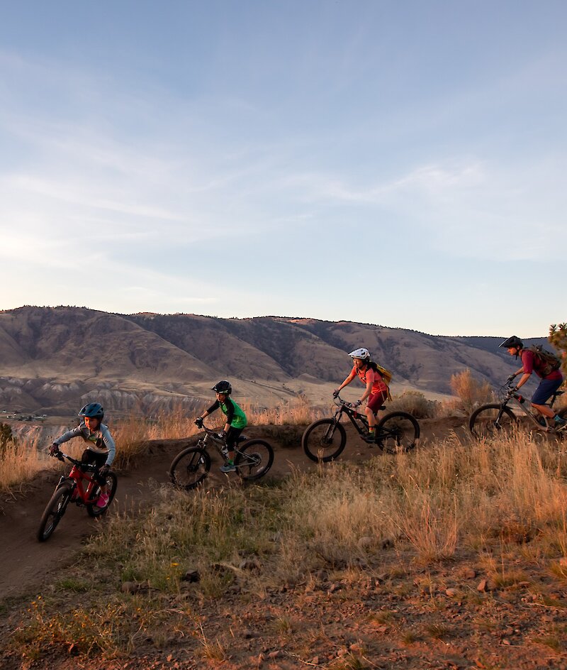 Family mountain biking along a bike trail at the Kamloops Bike Ranch with a view of the mountains in the background in Kamloops, British Columbia.