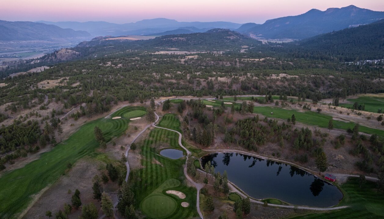 An aerial shot of Eaglepoint Golf Resort in Kamloops, with golf course features interspersed with an arid landscape. Blue hills and purple sunset light fill the background.