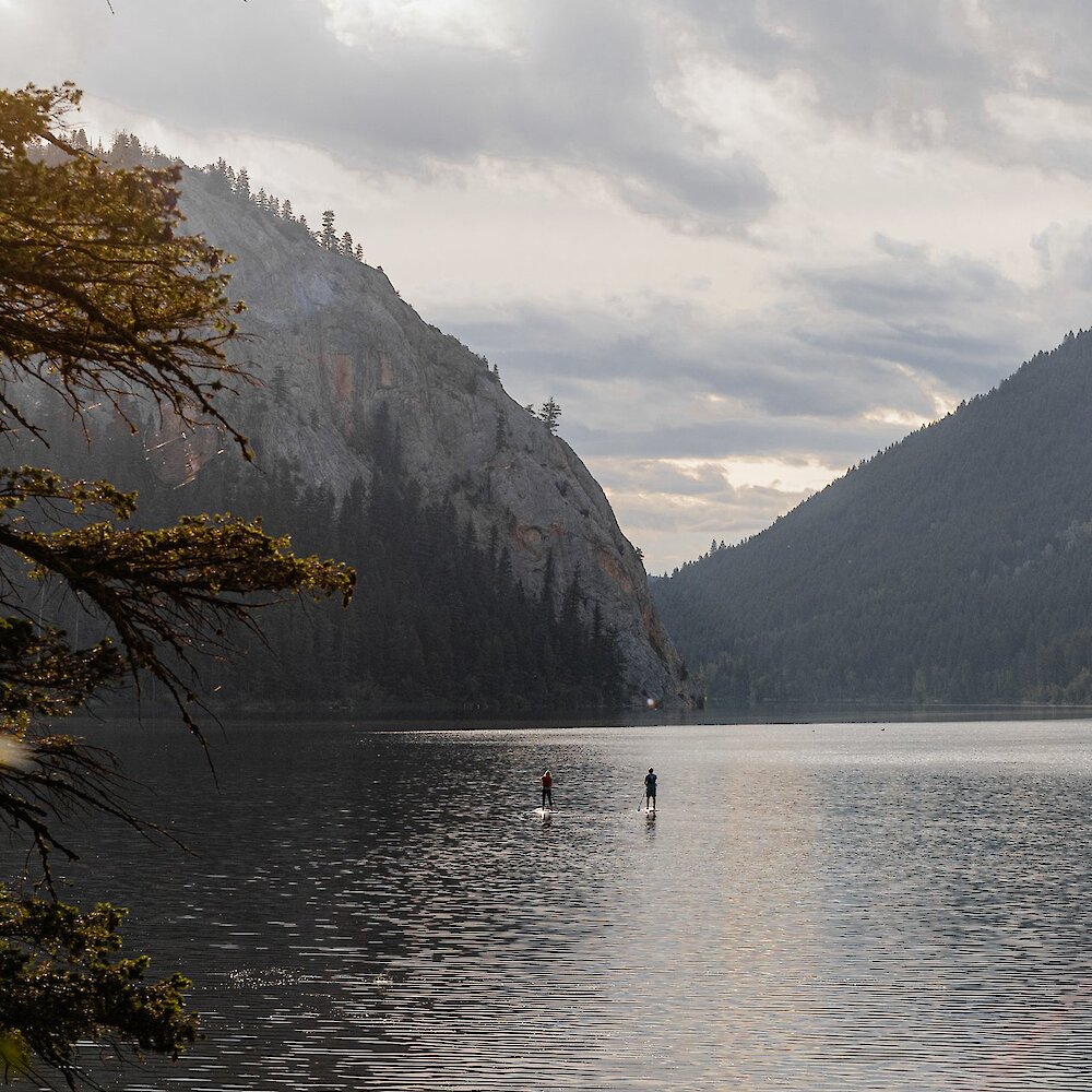 A couple paddleboarding on Paul Lake surrounded by nature located near Kamloops British Columbia.