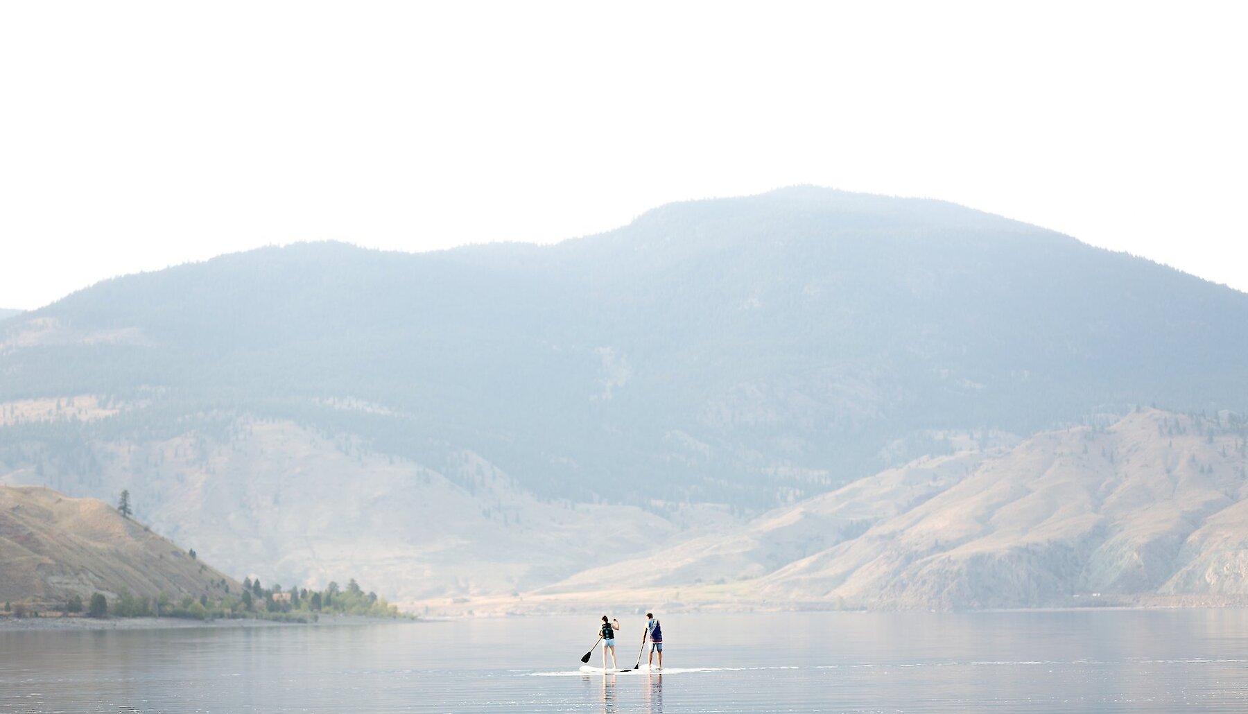 A couple on their paddleboards on Kamloops Lake with beautiful BC mountains in the background.