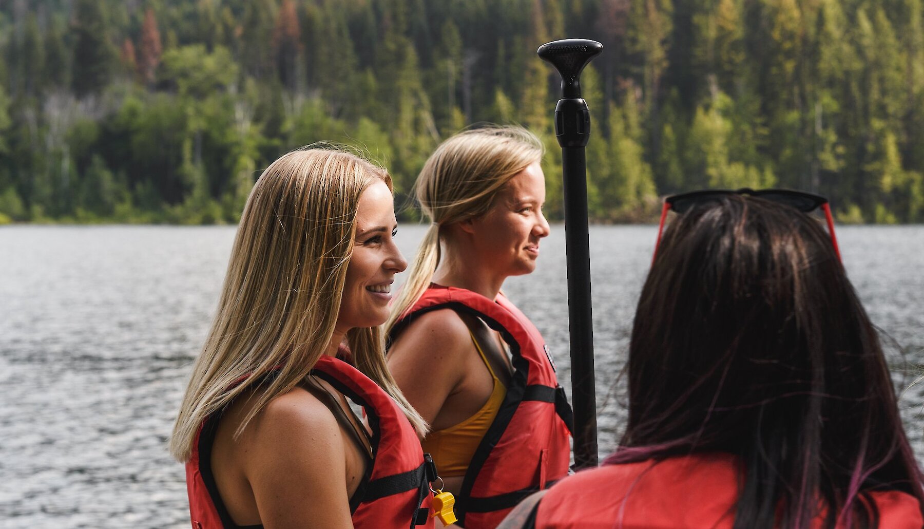 Three women wearing life jackets and holding their paddle before they head out on the lake near Kamloops, BC.