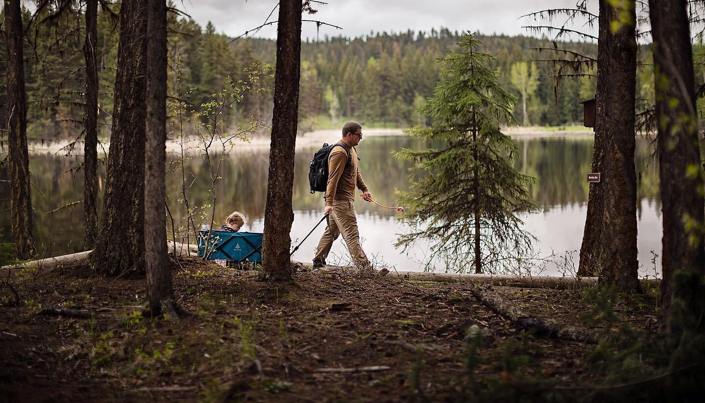 A young dad tows a wagon with a small child around Isobel Lake near Kamloops BC. It is a cool, misty autumn day.