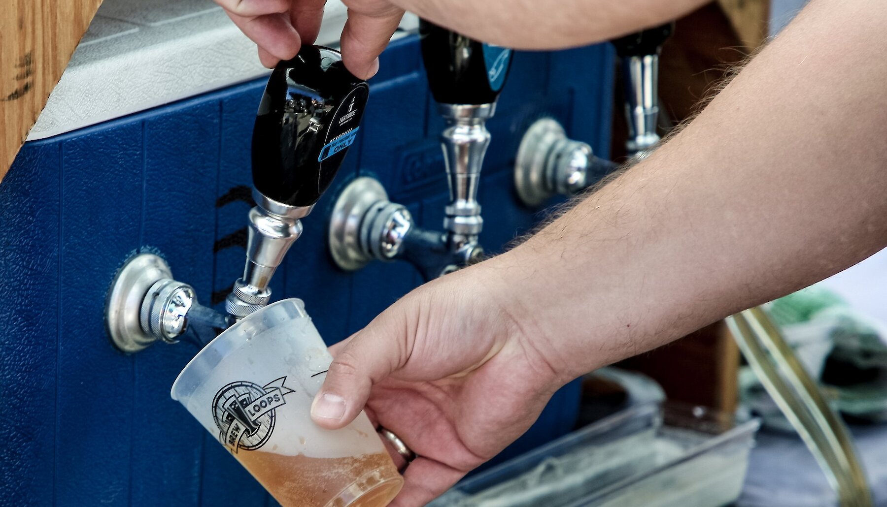 Someone fills a Brewloops-branded cup from a beer tap.