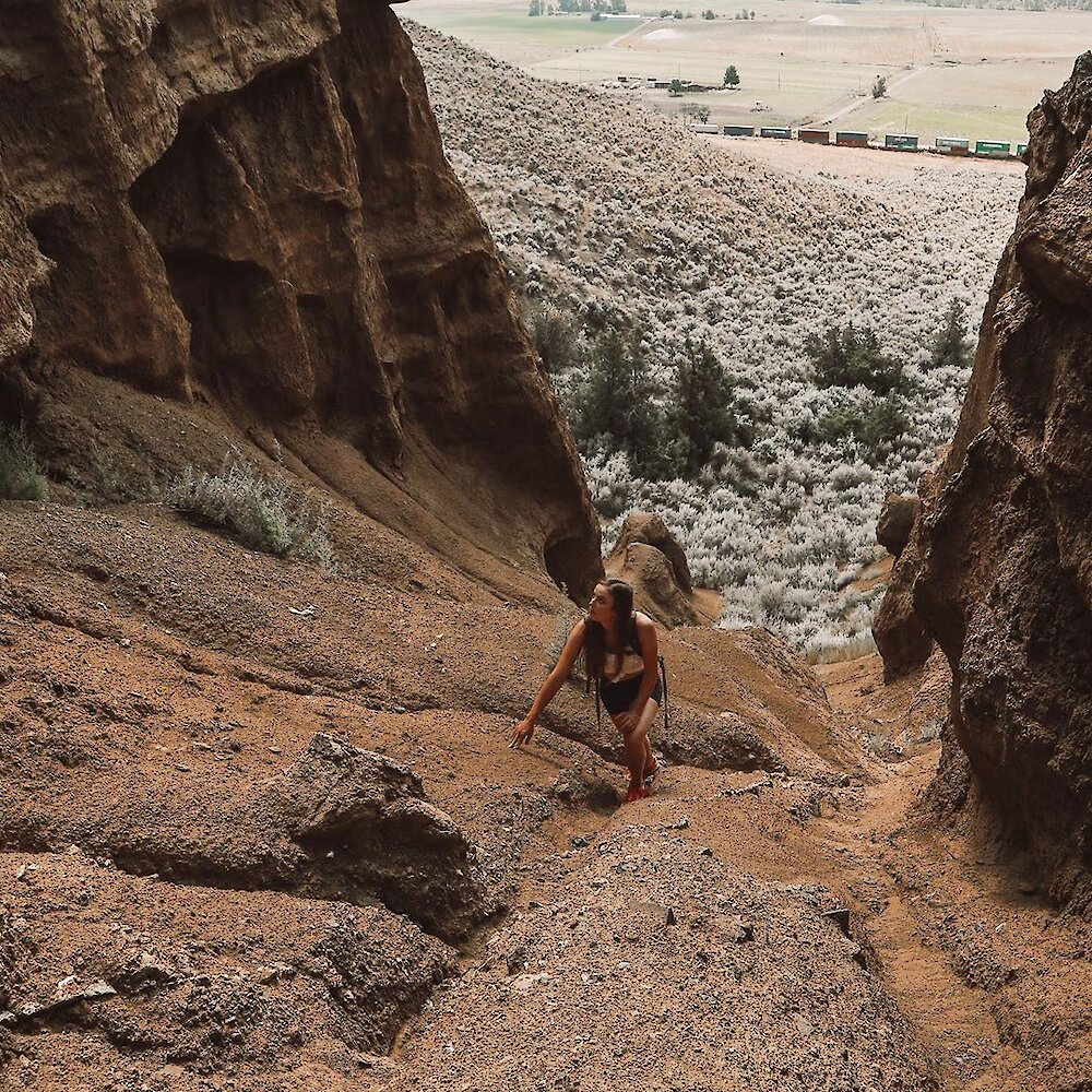 A hiker climbs a steep, narrow chasm between hoodoos.