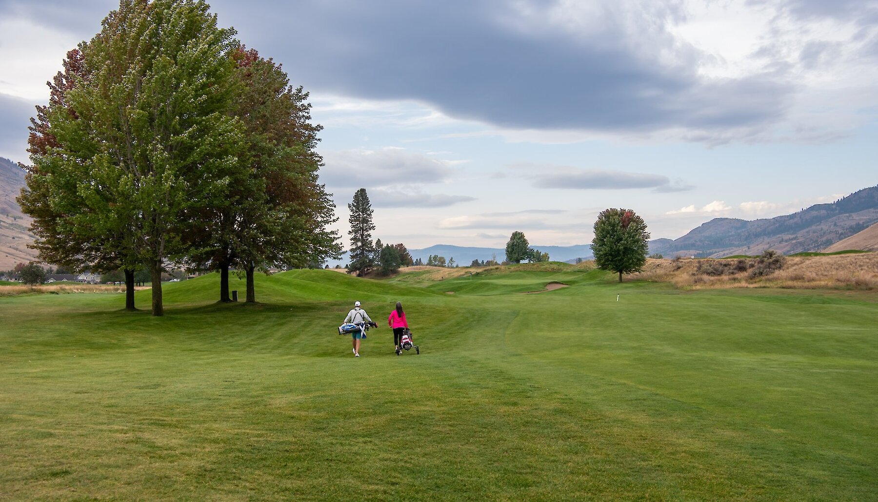 A couple with their golf clubs walking through the golf course at The Dunes at Kamloops, British Columbia.