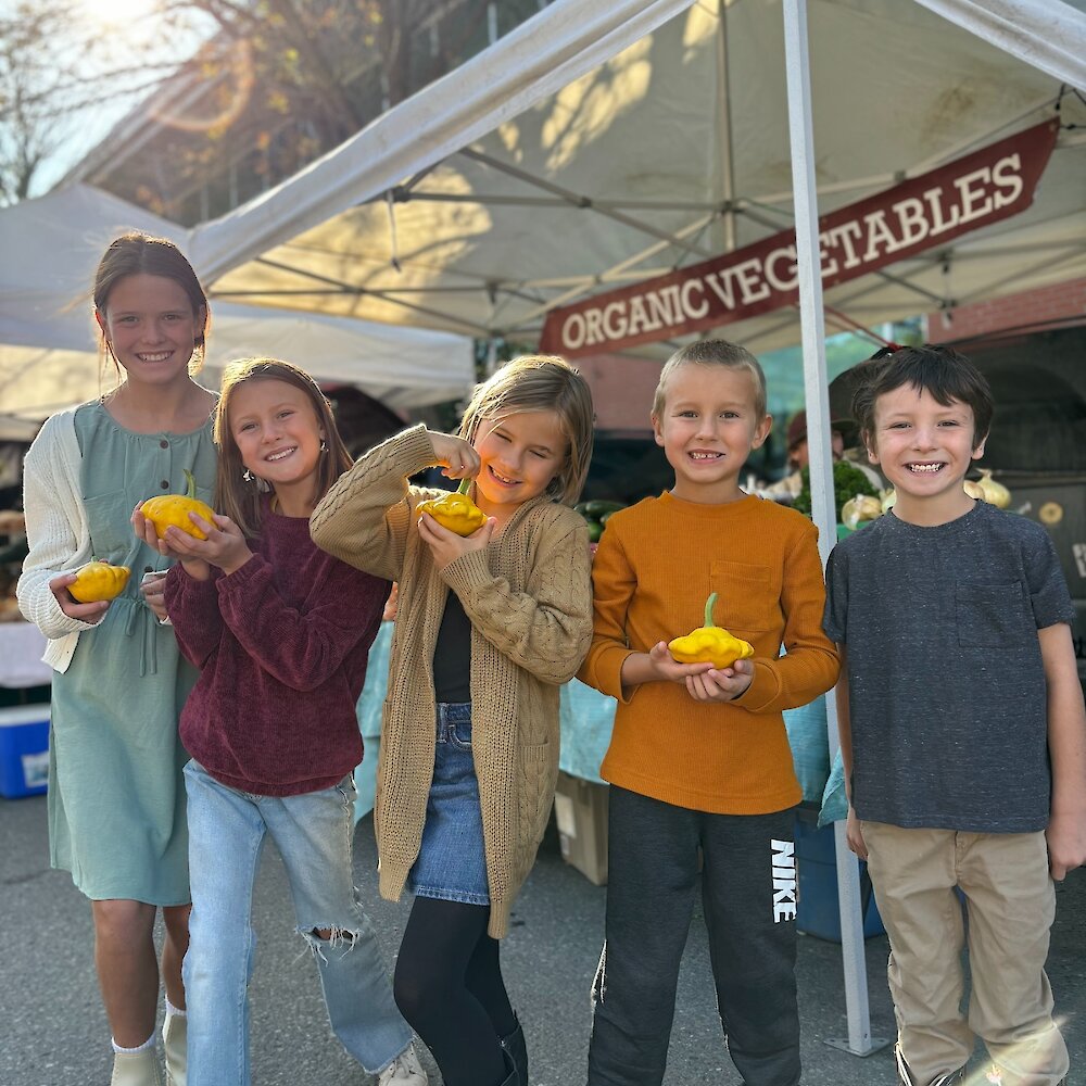 Kids posing with patty pan squash at the Kamloops Regional Farmers' Market during fall in British Columbia, Canada.