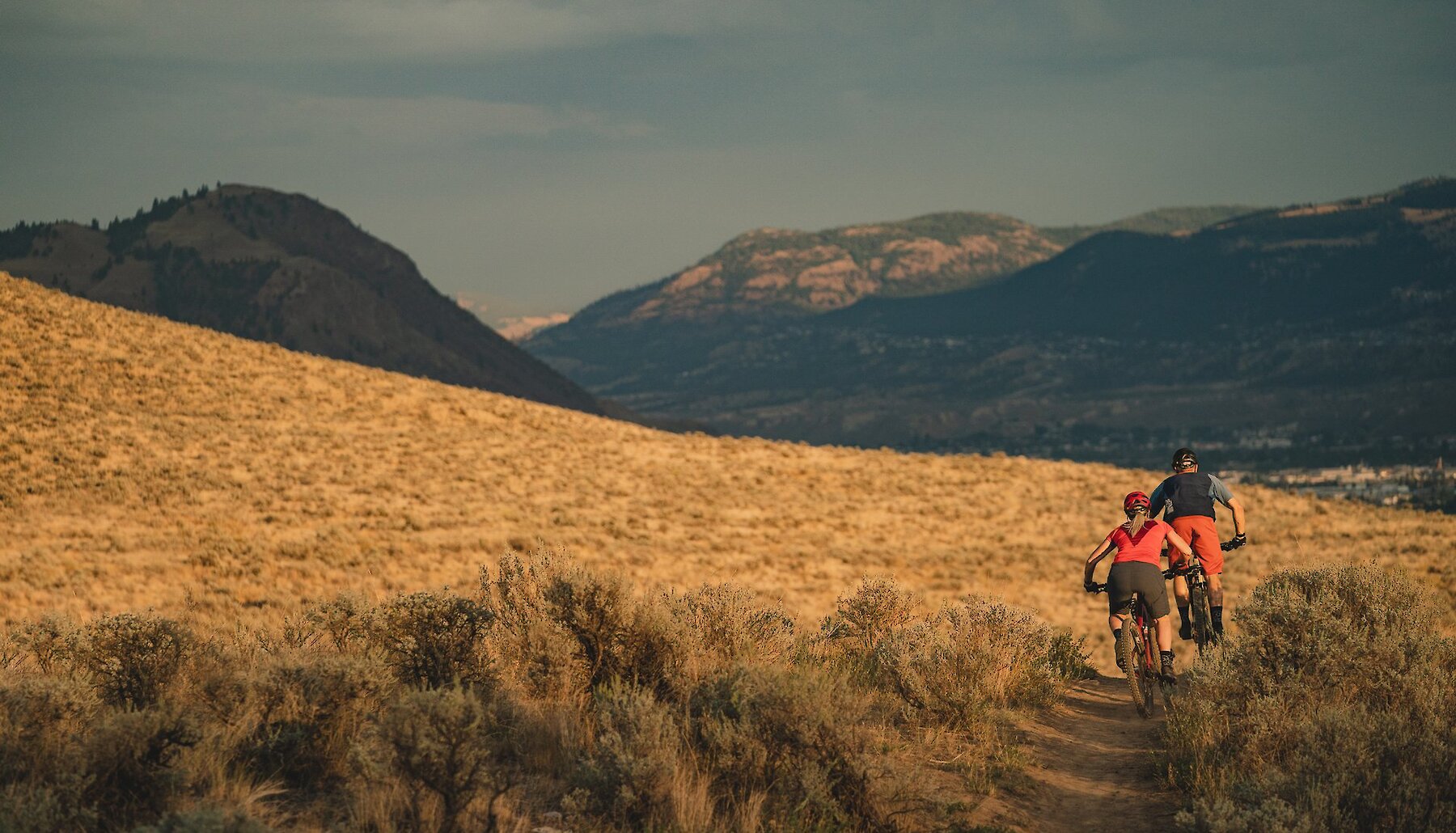 A couple mountain biking through the Lac du Bois Grasslands with scenic mountains in the background in Kamloops, British Columbia.