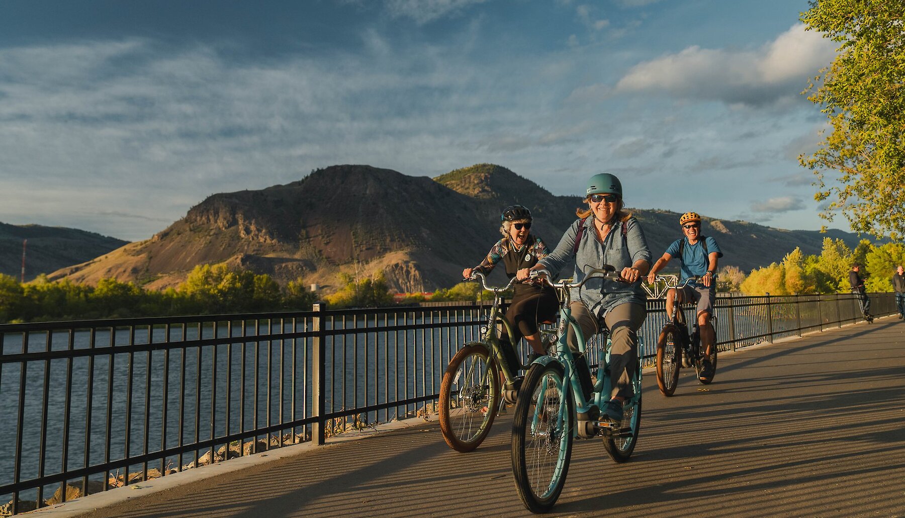 Group of visitors riding their ebikes along Riverside trail in Kamloops with the Thompson River and mountains in the background.