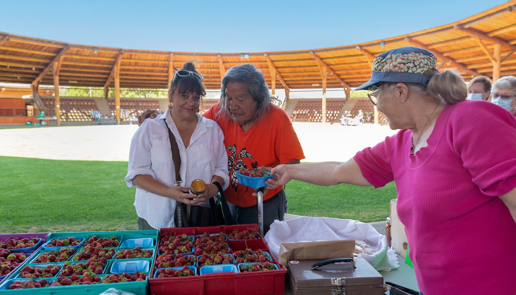 Vendor handing fresh local strawberries to visitor at the Kweseltken Farmers' and Artisan Market located on the Tk'emlúps Powwow Grounds.