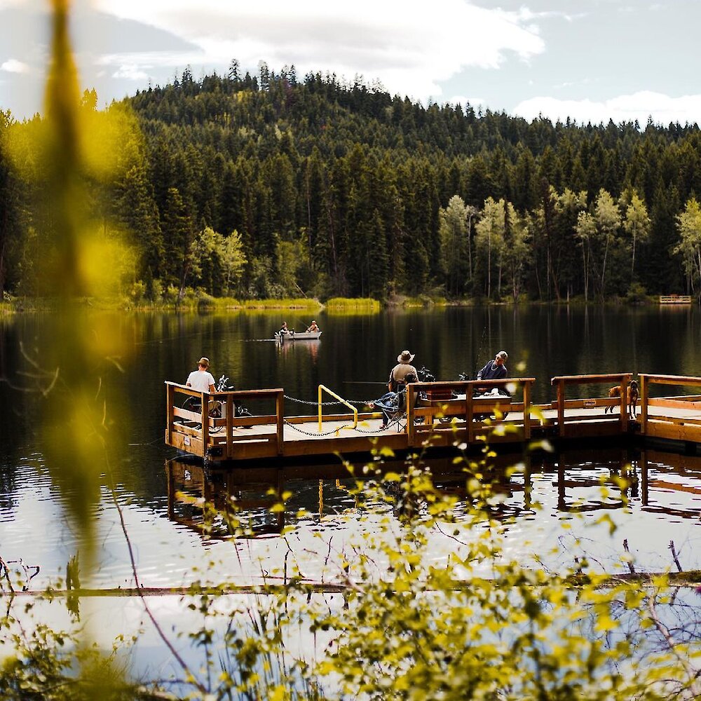 Group of fishermen using the dock for fishing and fishing boat in the water at Isobel Lake located near Kamloops, BC.