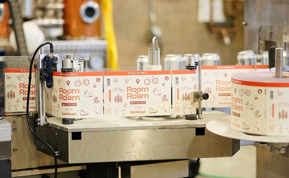 Labels of the Room to Roam beer can running through the production machine at Red Collar Brewing in Kamloops, BC.