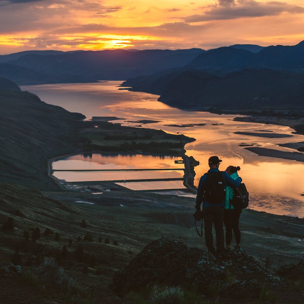 A couple admiring the stunning views of the sunset hiking at Kenna Cartwright Nature Park in Kamloops, British Columbia.